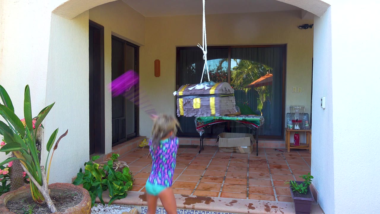 In San Jose Del Cabo, the child follows through with the purple stick while the treasure-chest piñata swings right under the patio roof.