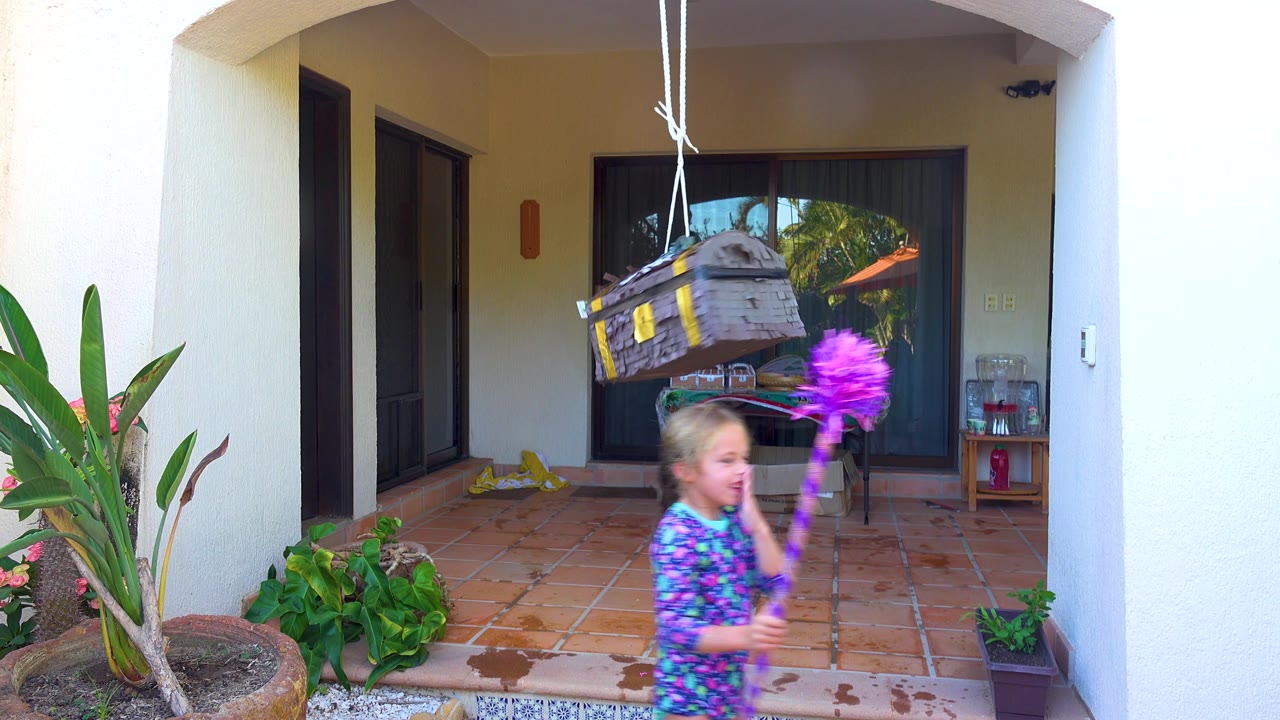 The child passes under the hanging piñata on the San Jose Del Cabo patio while the decorated box tilts and swings above the tiled floor.