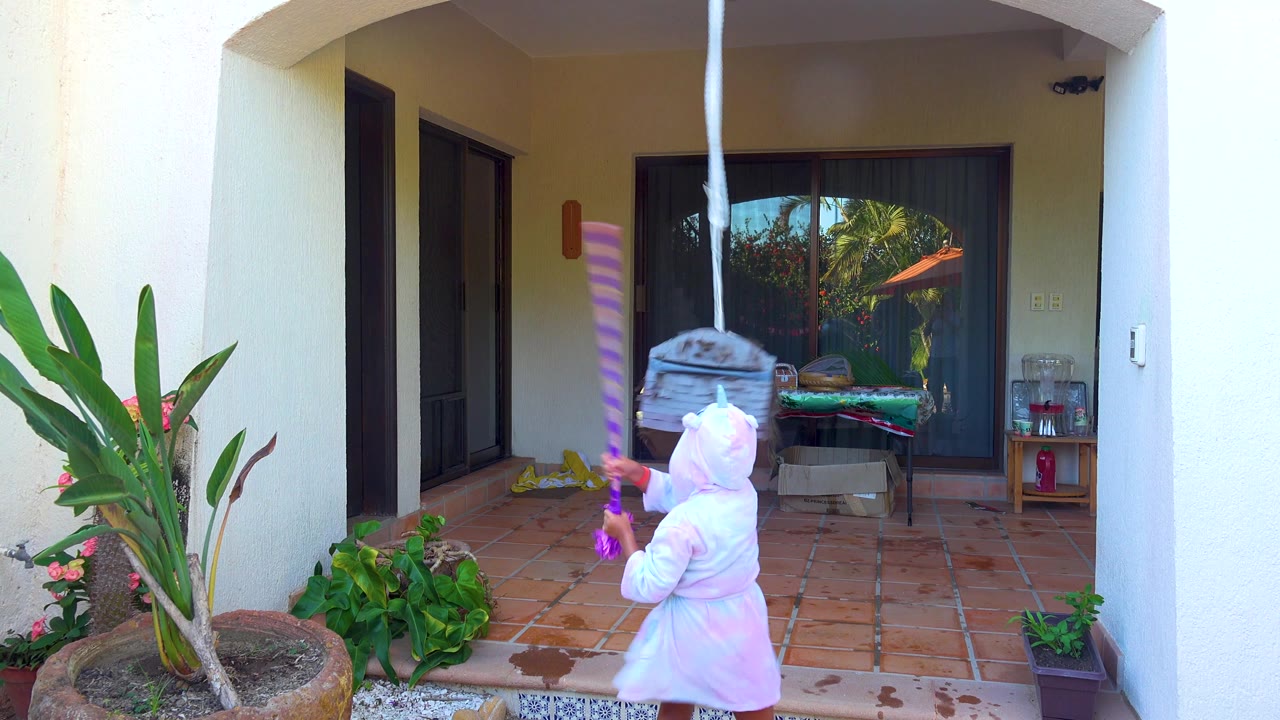 Child swings a purple stick upward toward the hanging piñata.