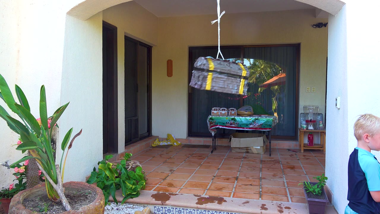 Child approaches a hanging pinata on a tiled patio.