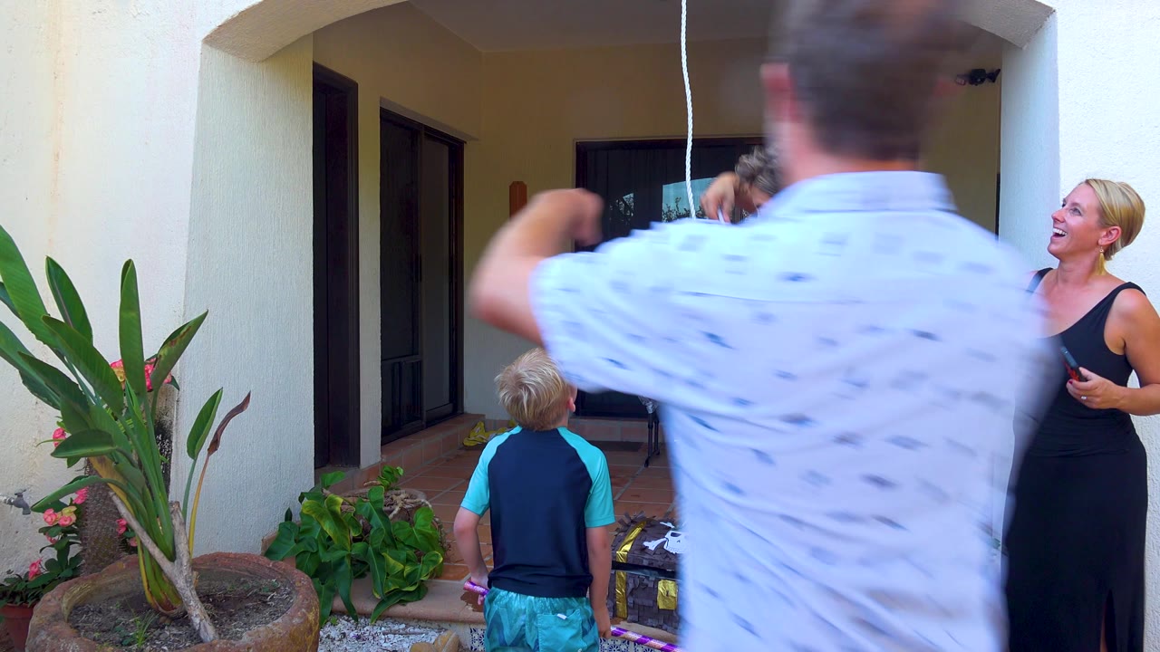 A man passes in front of a child and woman on a shaded patio.