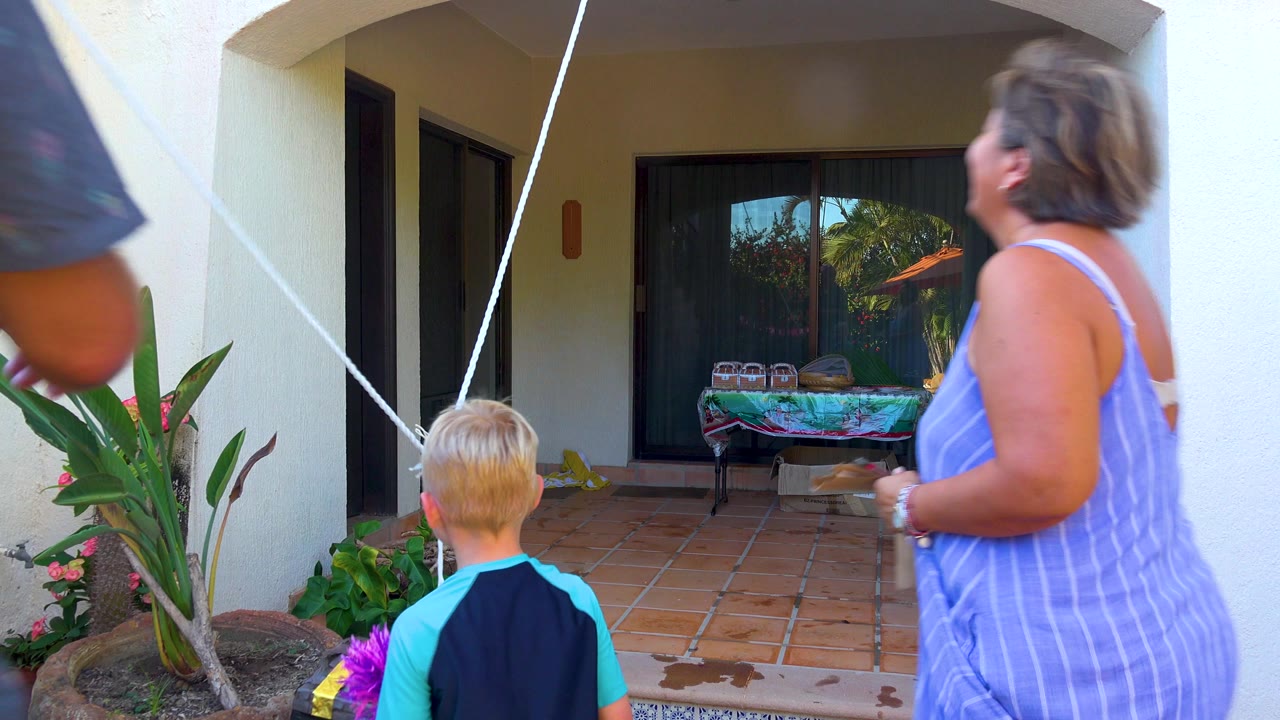 At the start of the San Jose del Cabo clip, a woman in a striped blue dress and a blond child stand on a tiled patio while a white rope angles across the frame.