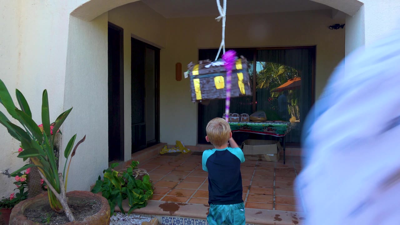 Child stands under piñata while a blurred adult passes near the camera.
