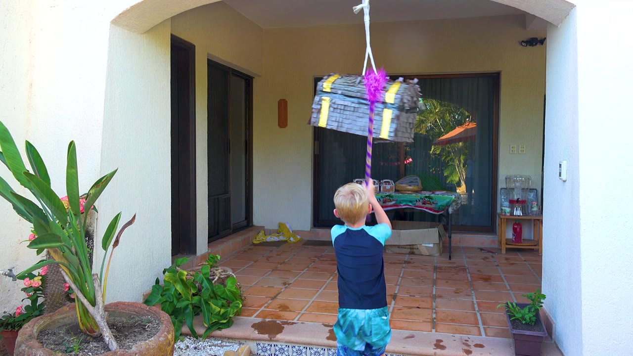 Child swings a pink stick toward a hanging piñata.