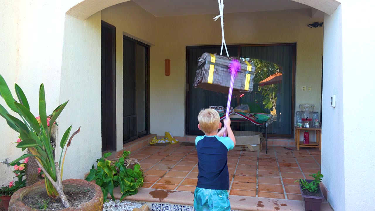 The piñata has shifted to the upper right while the child keeps the pink stick raised in the San Jose Del Cabo courtyard.