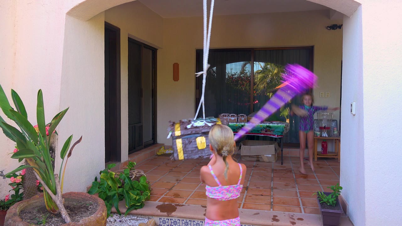 Purple stick blurs toward a hanging piñata while another child watches.