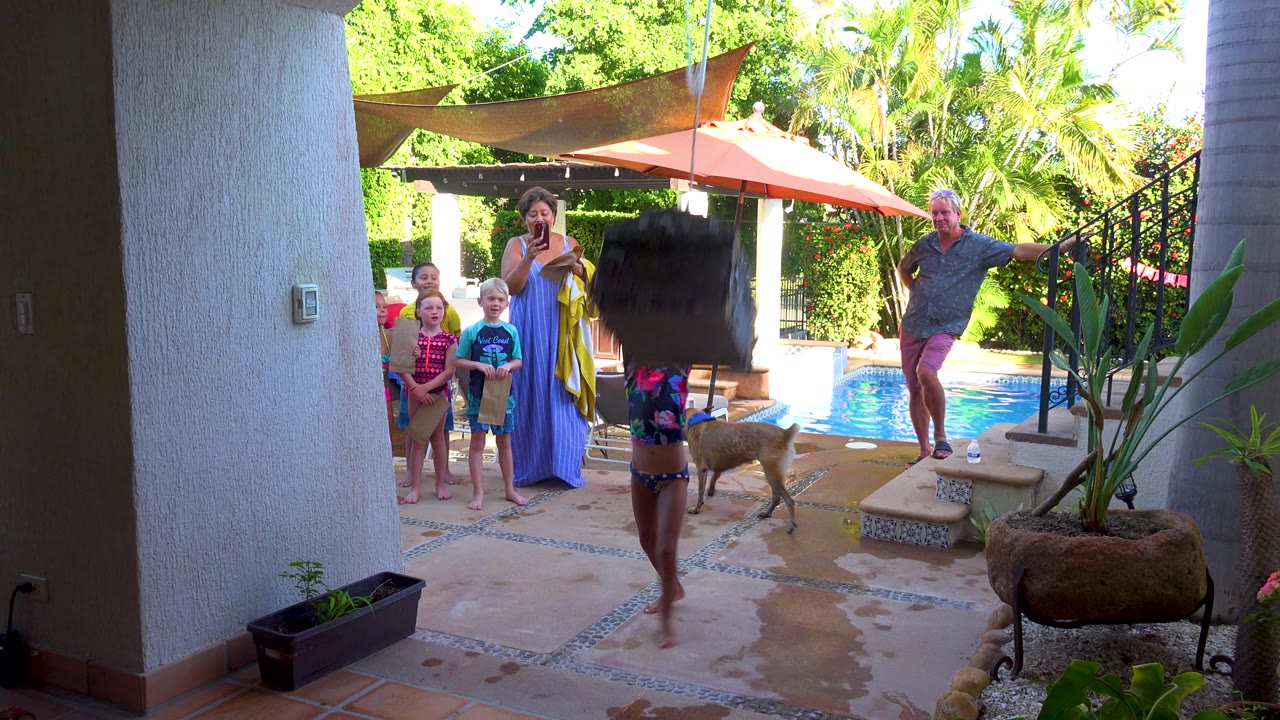 Child begins raising the black toy while people watch near the pool.