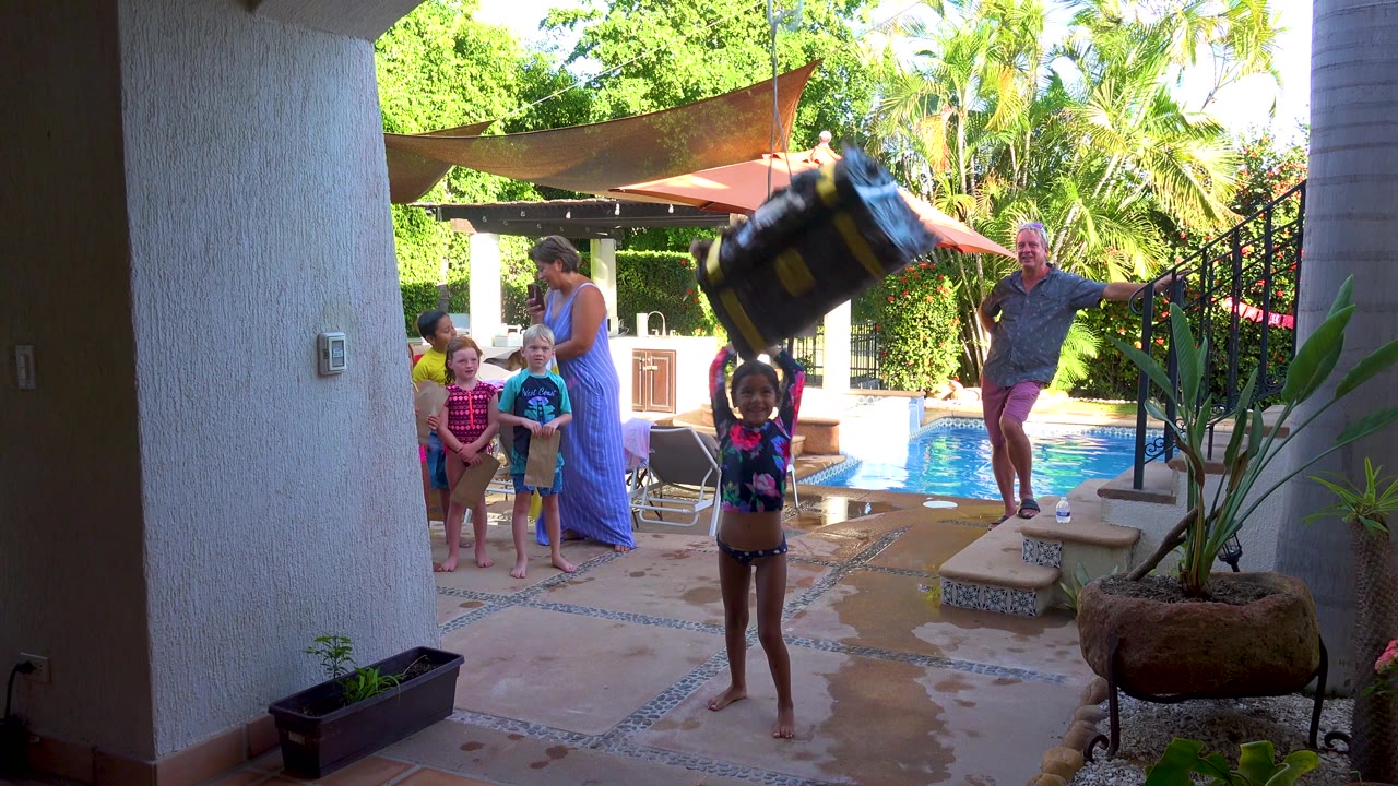 Child holds the large bag overhead near the swimming pool with adults and children behind.