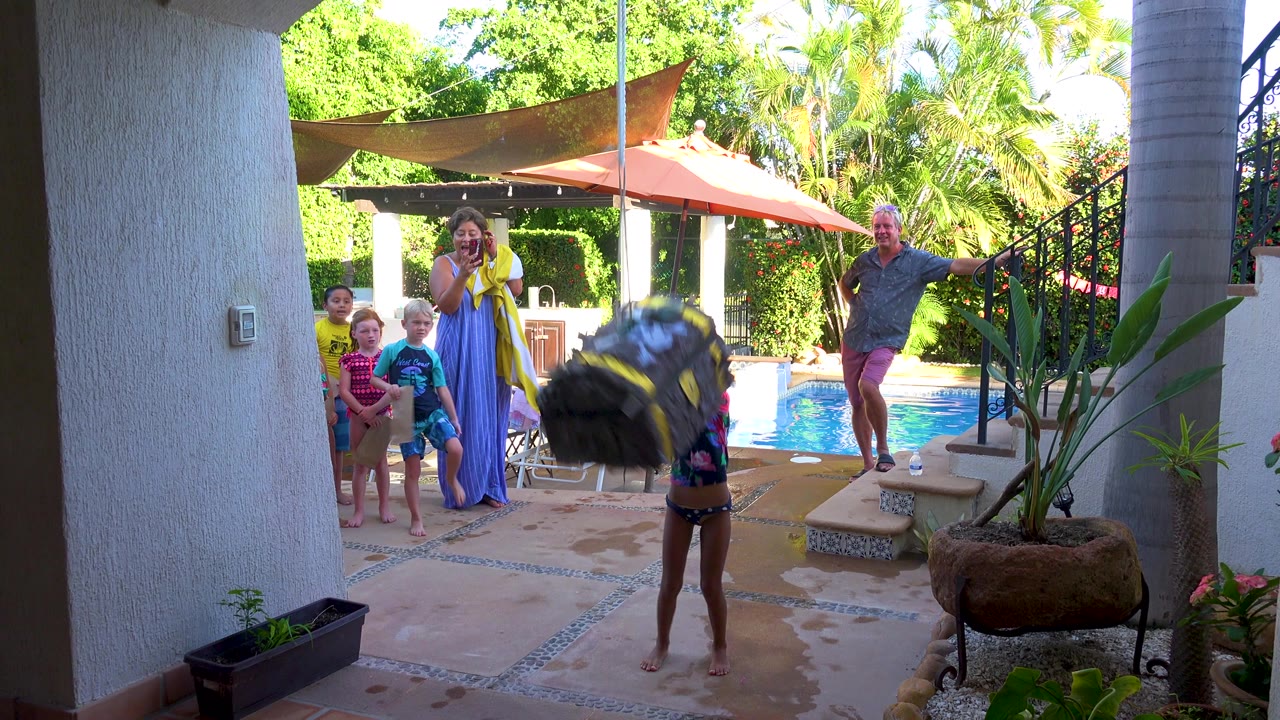 In San Jose del Cabo, a child stands under a hanging tire swing on a wet backyard patio while children and adults watch beside a pool and shaded seating area.