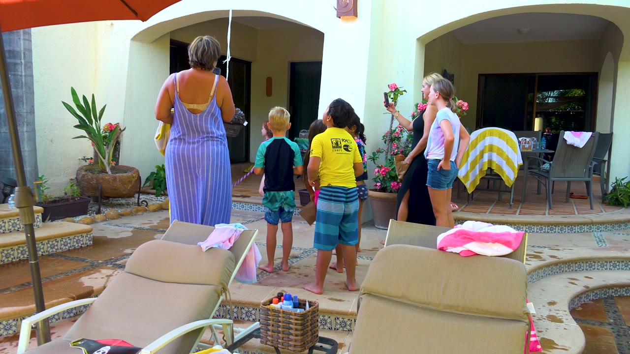 Group on patio with a woman holding flowers beside children near the pool.
