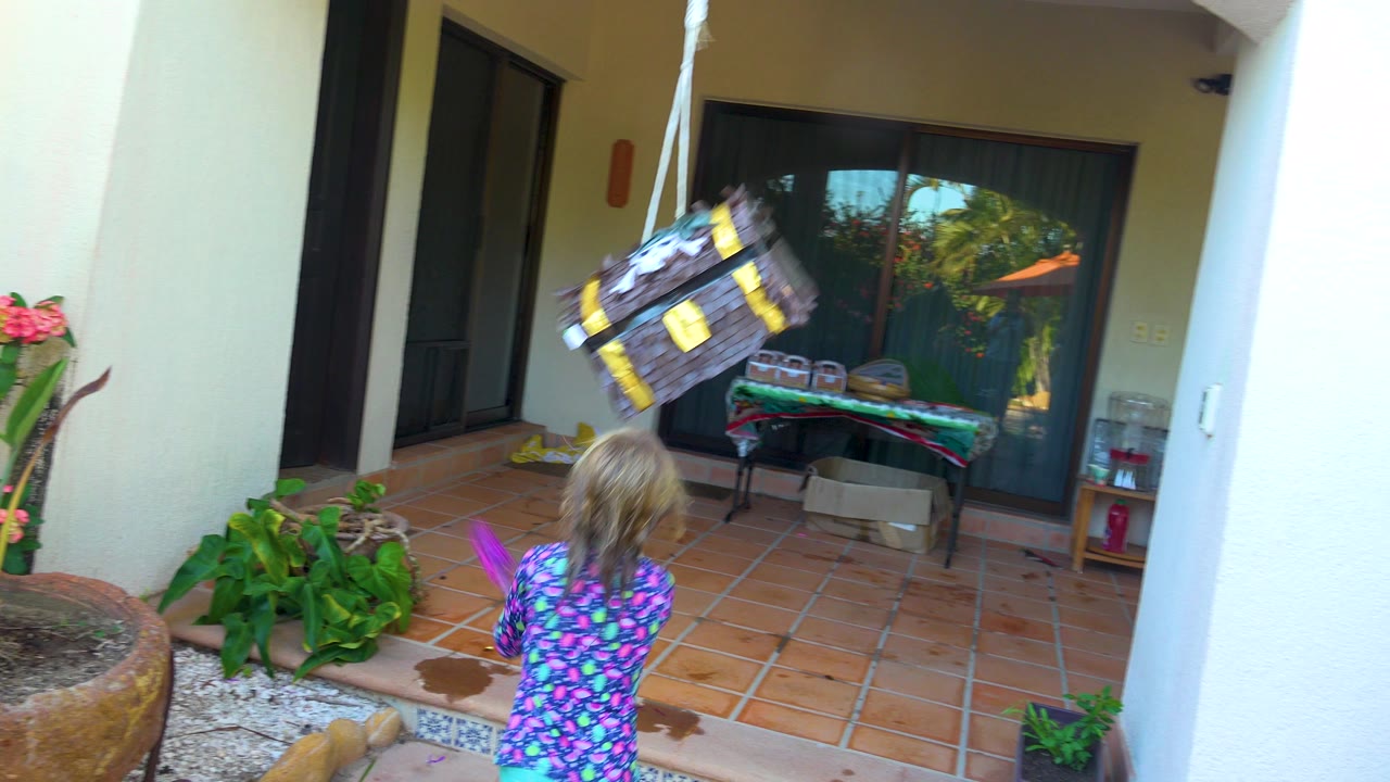 In San Jose Del Cabo, the piñata swings across the upper frame as the child stands below it on the tiled patio with the pink stick visible near their side.