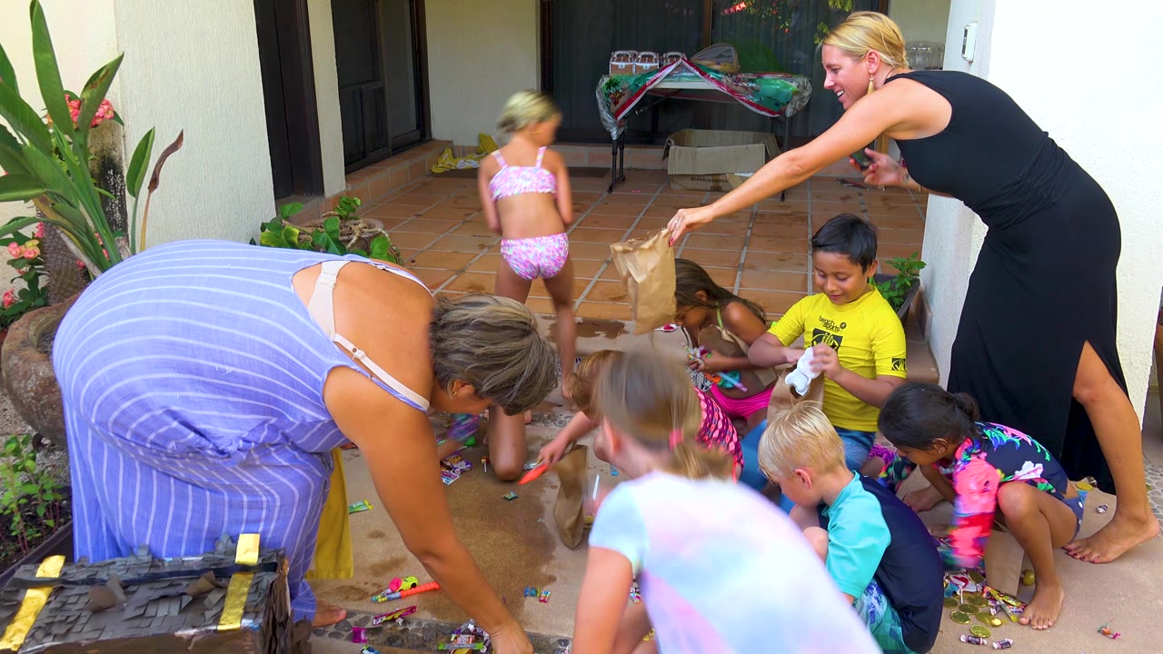 Adult reaches a bag toward children sitting on the patio.