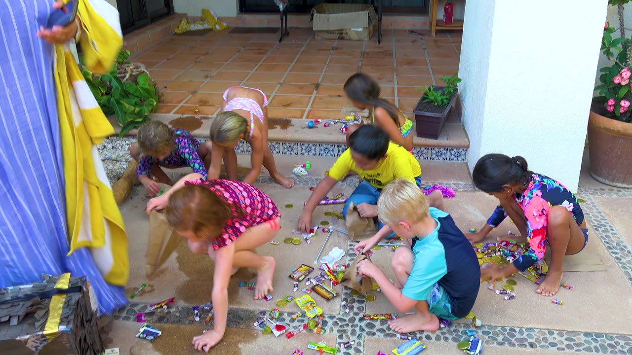 Children gather candies from a wet patio near potted plants and doorway steps.