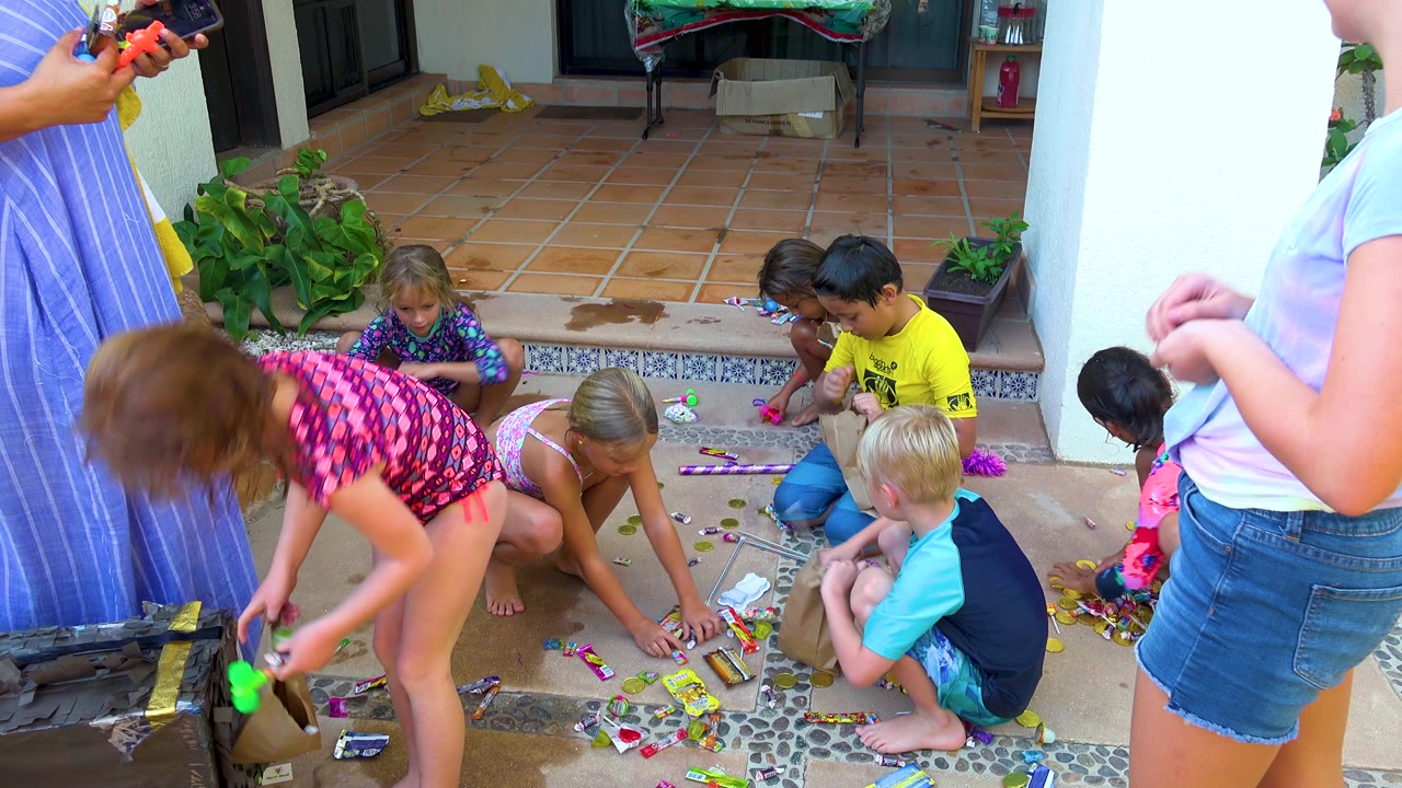 A child in pink patterned swimwear reaches with a small bag while other children collect candies across the patio in San Jose Del Cabo, Mexico.