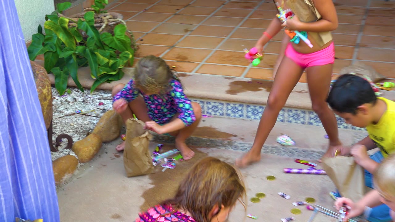 Children in swimwear play with water guns beside a brown paper bag on a wet tiled pool deck in San Jose del Cabo, Mexico.