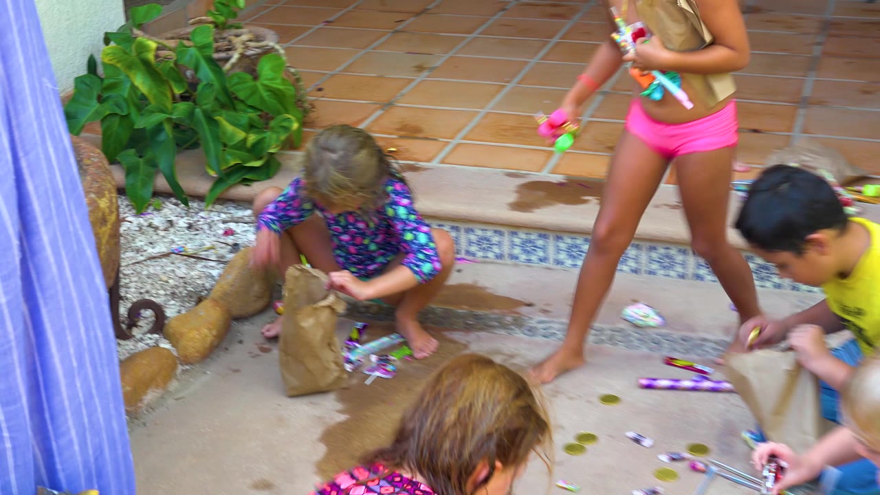 Children continue playing with water guns around a paper bag.