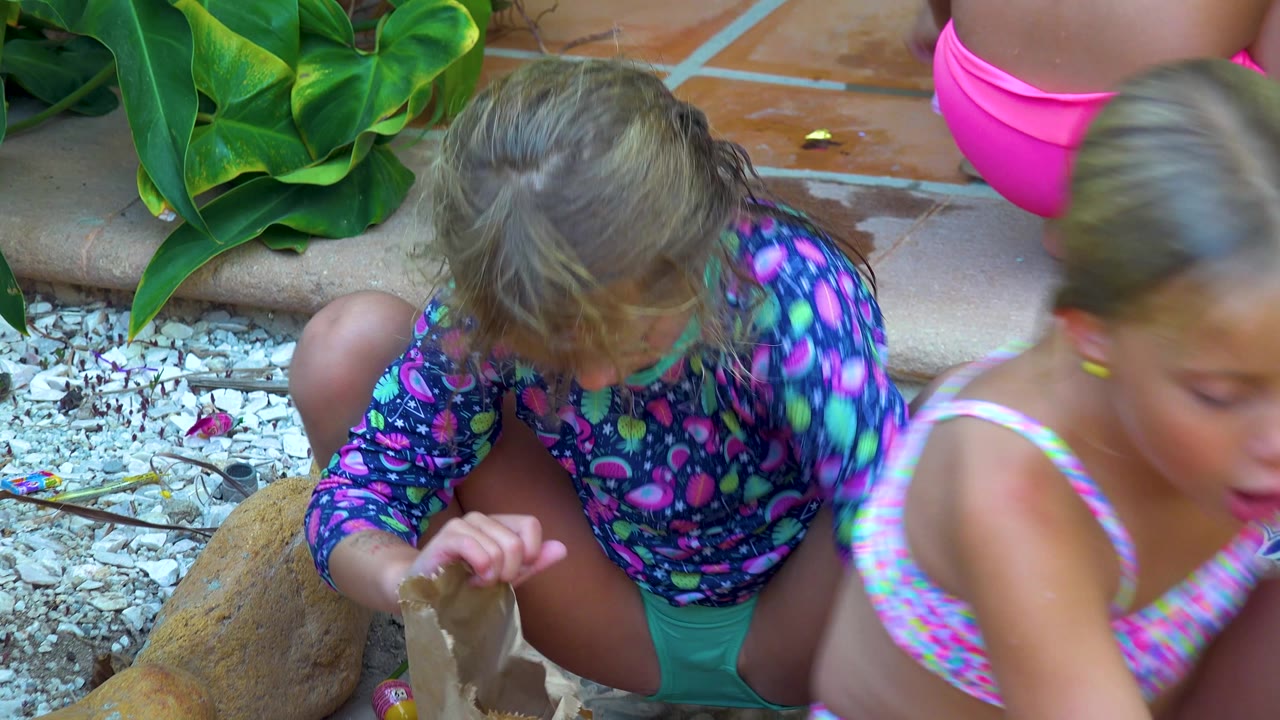 A child crouches over a paper bag as another child passes in front.