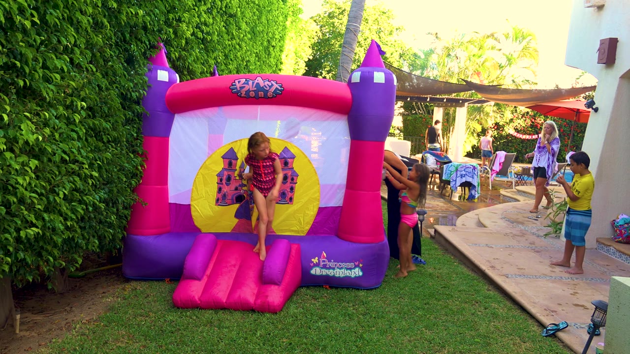 The girl leans forward on the pink inflatable step as children and adults remain visible around the patio in a San Jose del Cabo backyard party scene.