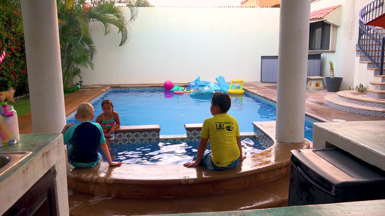 Children remain seated beside the pool as floating toys drift near the far wall.