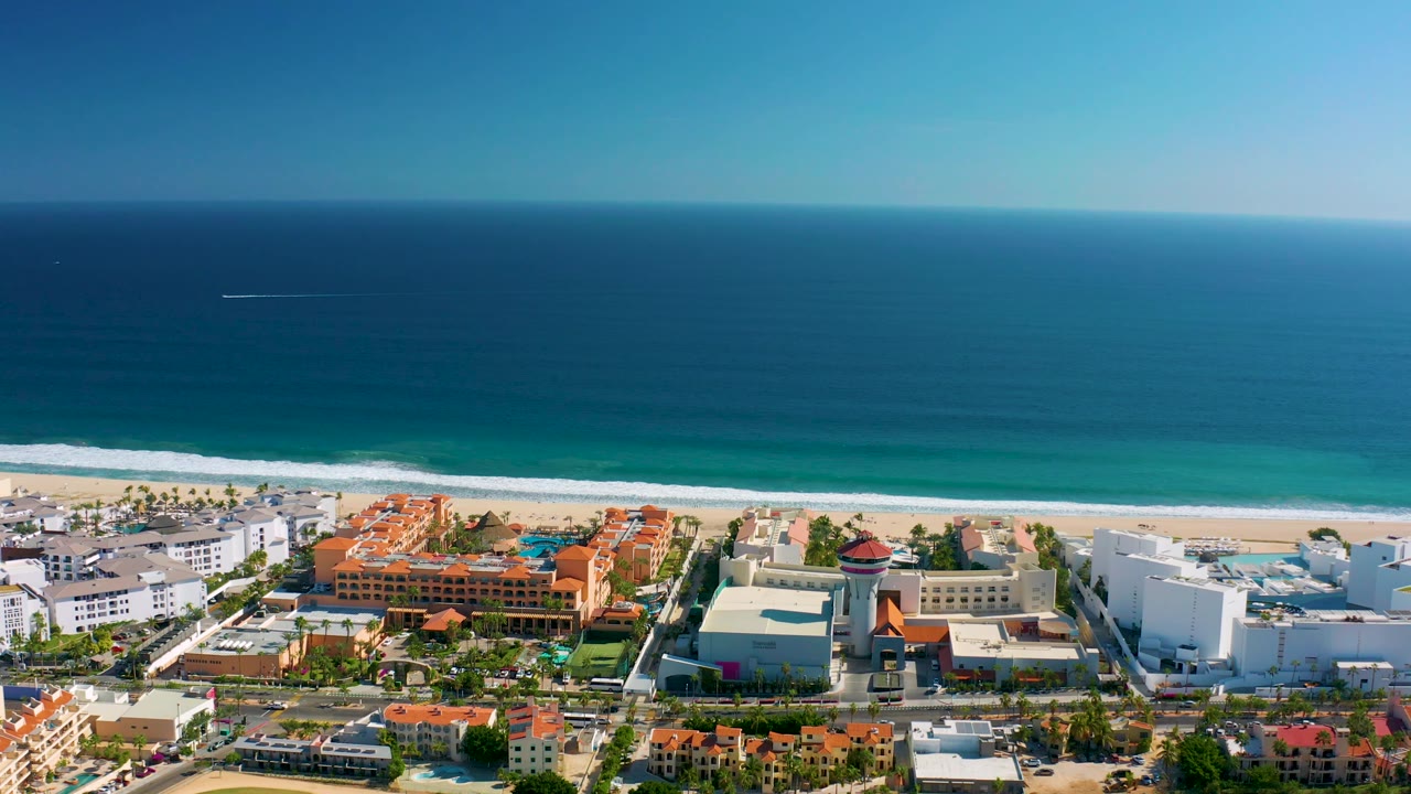 Third frame presents blue water across the upper view, a bright white wave line on the San Jose del Cabo beach, clustered coastal architecture, and no visible people.