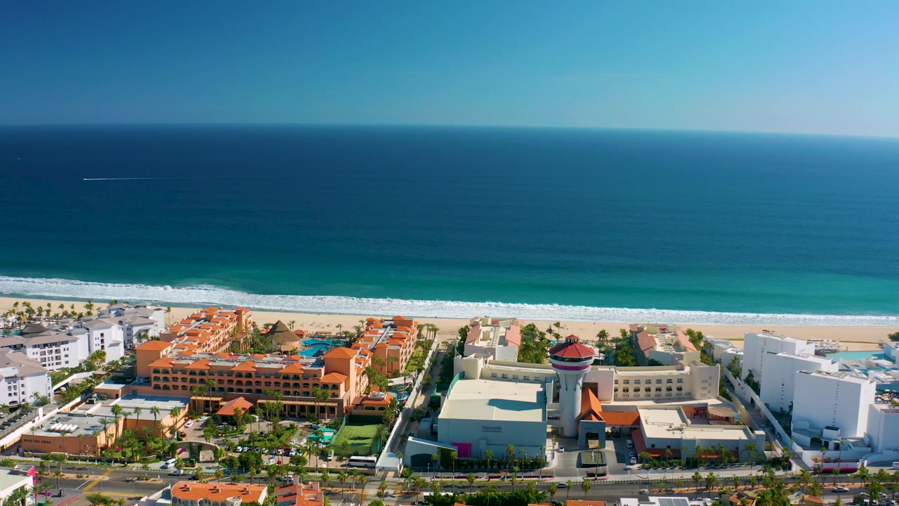 San Jose del Cabo aerial view with the beach and moving wave foam stretching across the frame above hotels, landscaped areas, and no visible people.