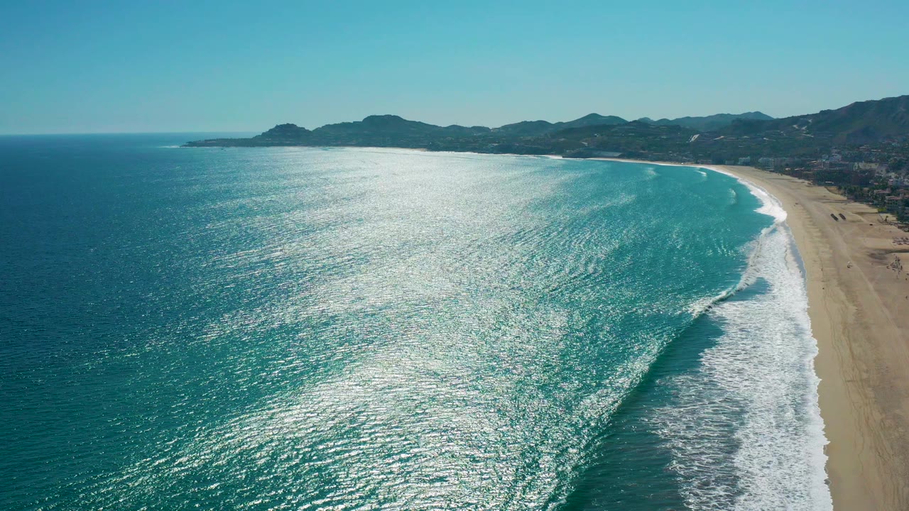 Aerial view of turquoise waves breaking beside a sandy beach.
