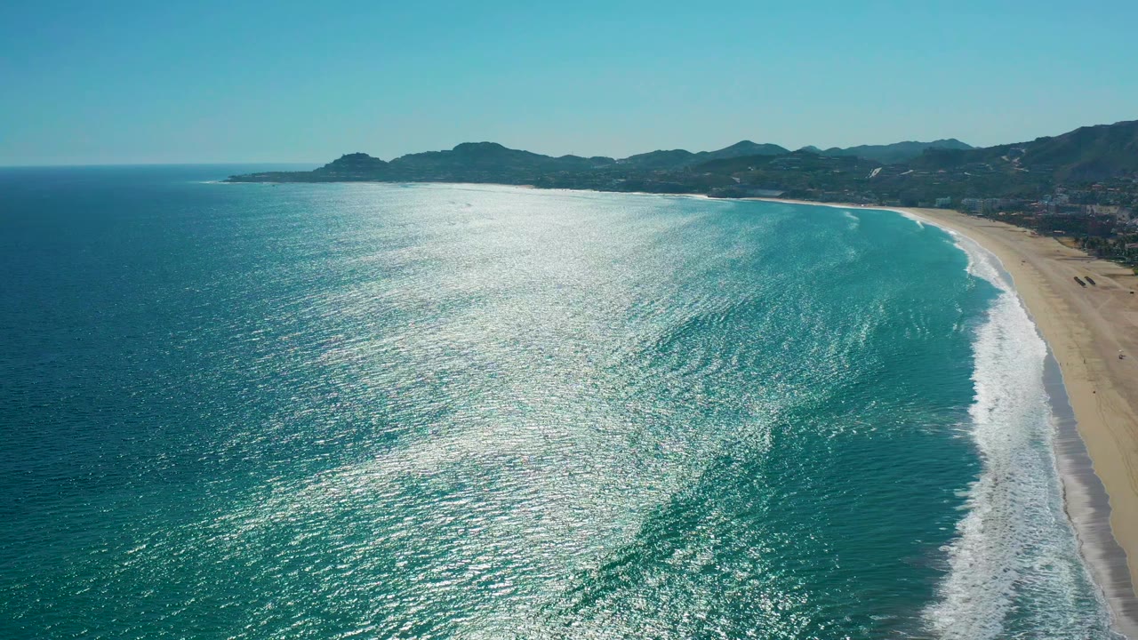 Sunlit water shimmers across the center of the San Jose del Cabo aerial view while the beach curves along the right side and no visible people appear on the sand.