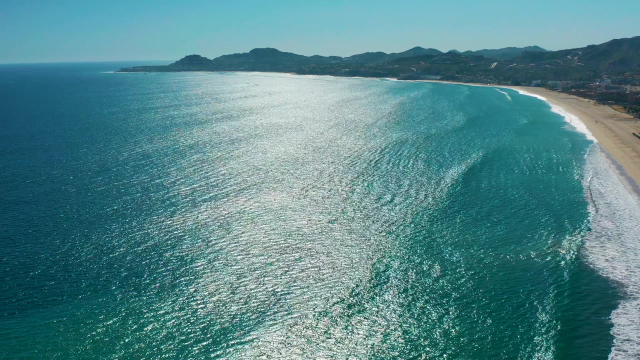 Aerial coastal water with white surf curling toward a sandy beach
