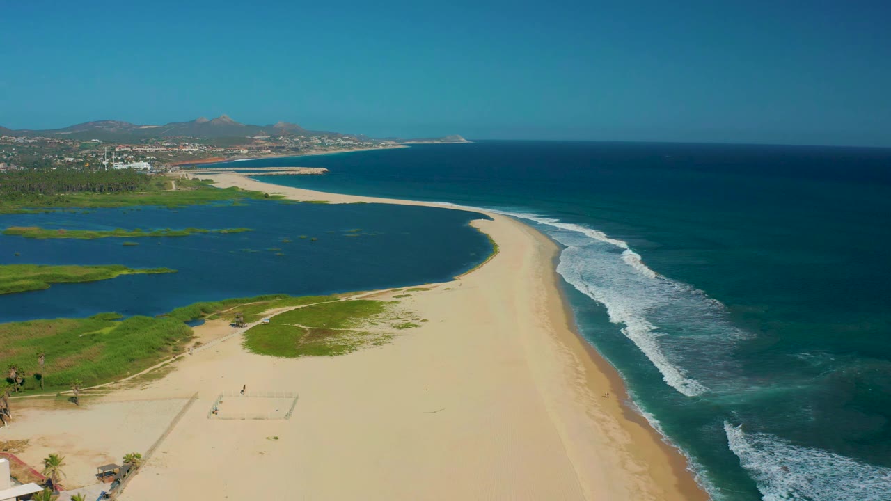 Wide beach aerial with lagoon on the left and surf on the right.