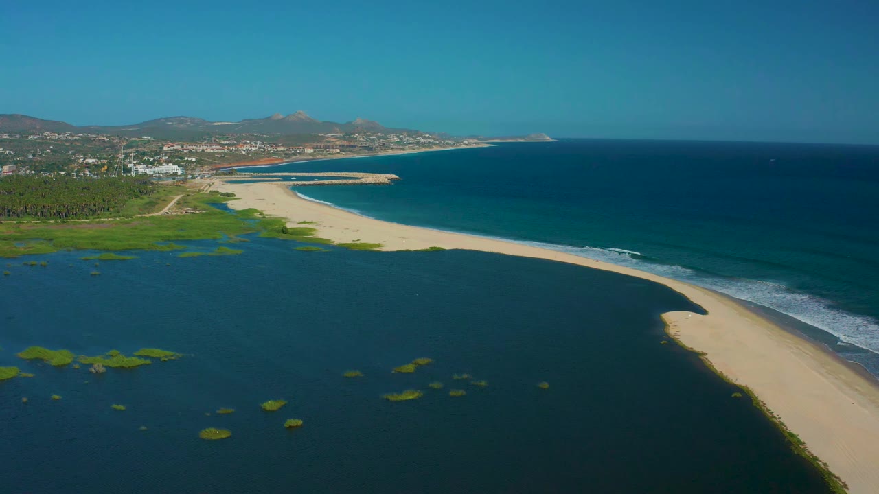 Wide aerial coastline with lagoon patches, sand beach, and ocean surf.