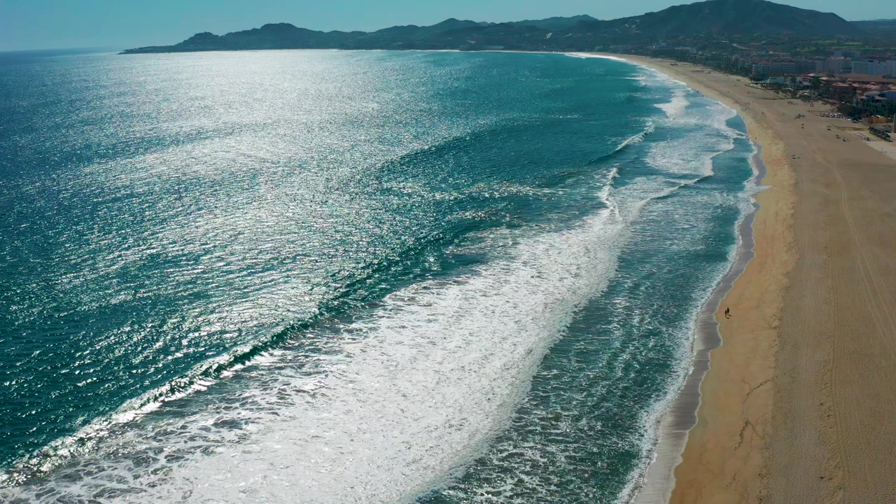 Aerial coastal view with foamy waves spreading across the shoreline.