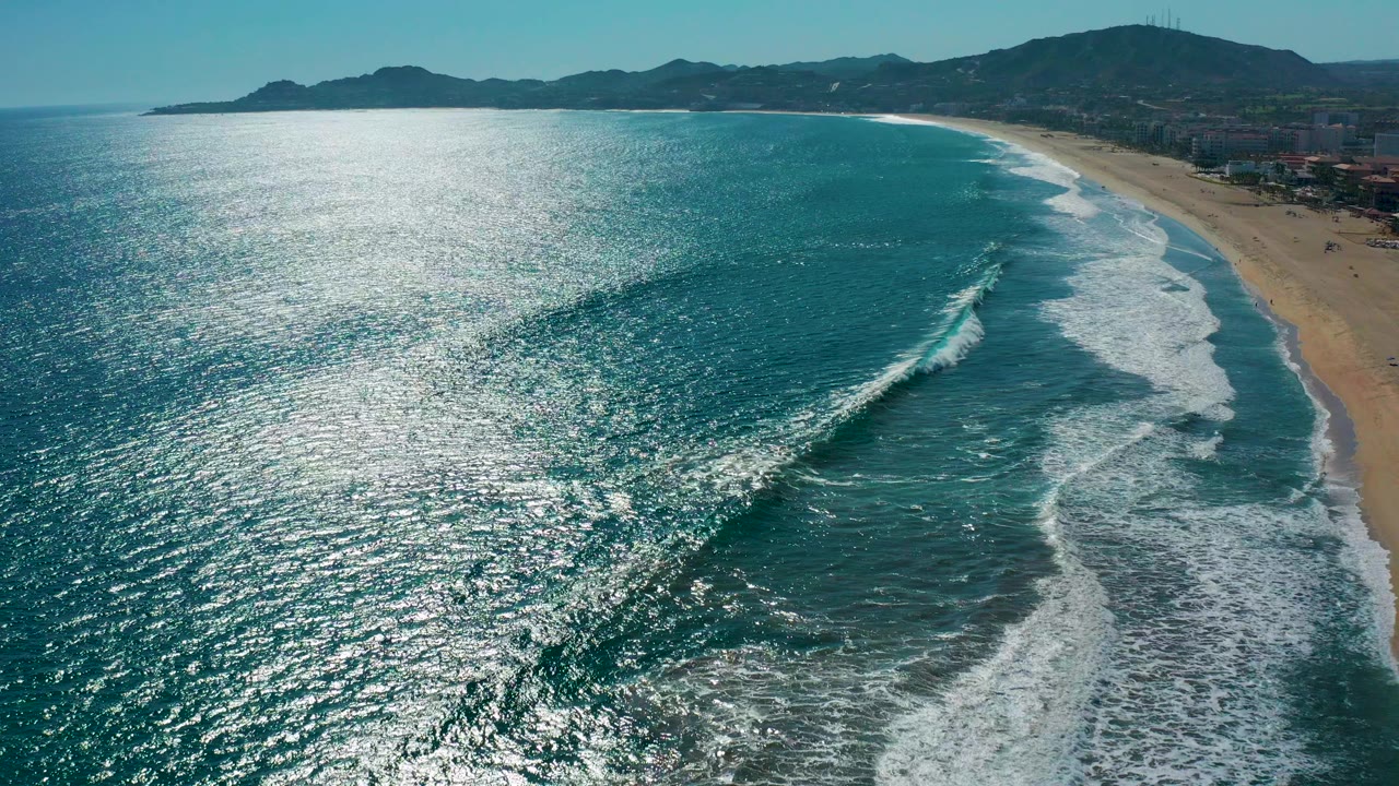 Aerial view of turquoise surf rolling toward a sandy beach