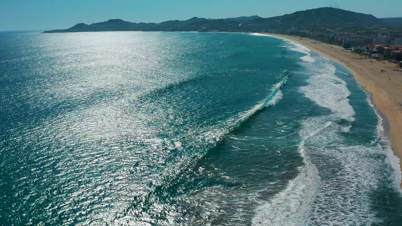 Aerial San Jose del Cabo beach view with a diagonal wave crest breaking through blue-green water beside the sandy shoreline and no visible people.