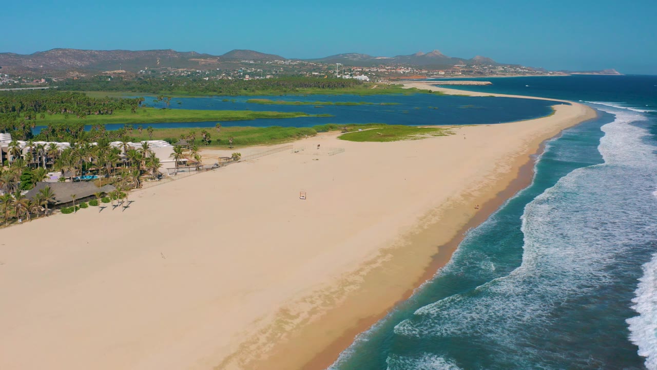 Aerial beach view with ocean surf, lagoon, green coast, palms, and hills.