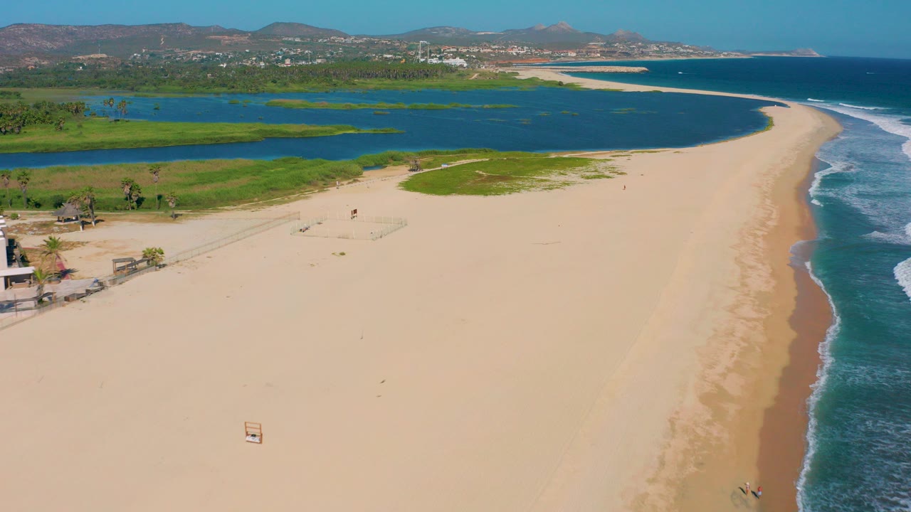Aerial view of a sandy beach between a lagoon and ocean surf.