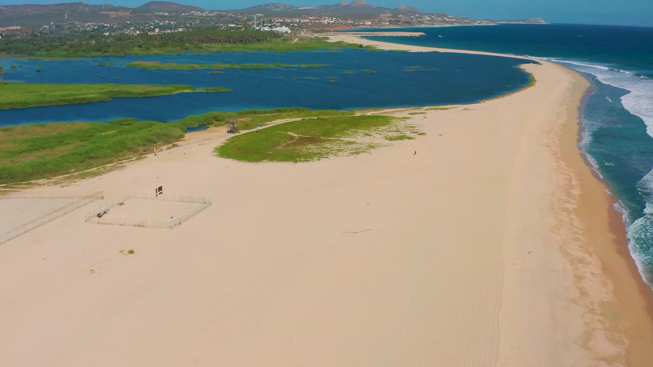 Wide beach aerial with lagoon, surf, and distant hills.