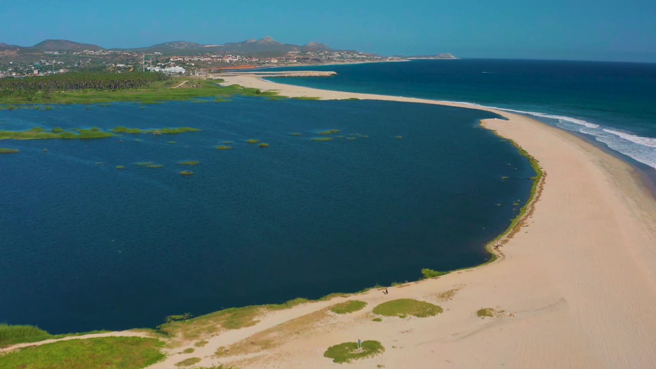 Lagoon beside a long sandy beach with ocean and hills beyond.