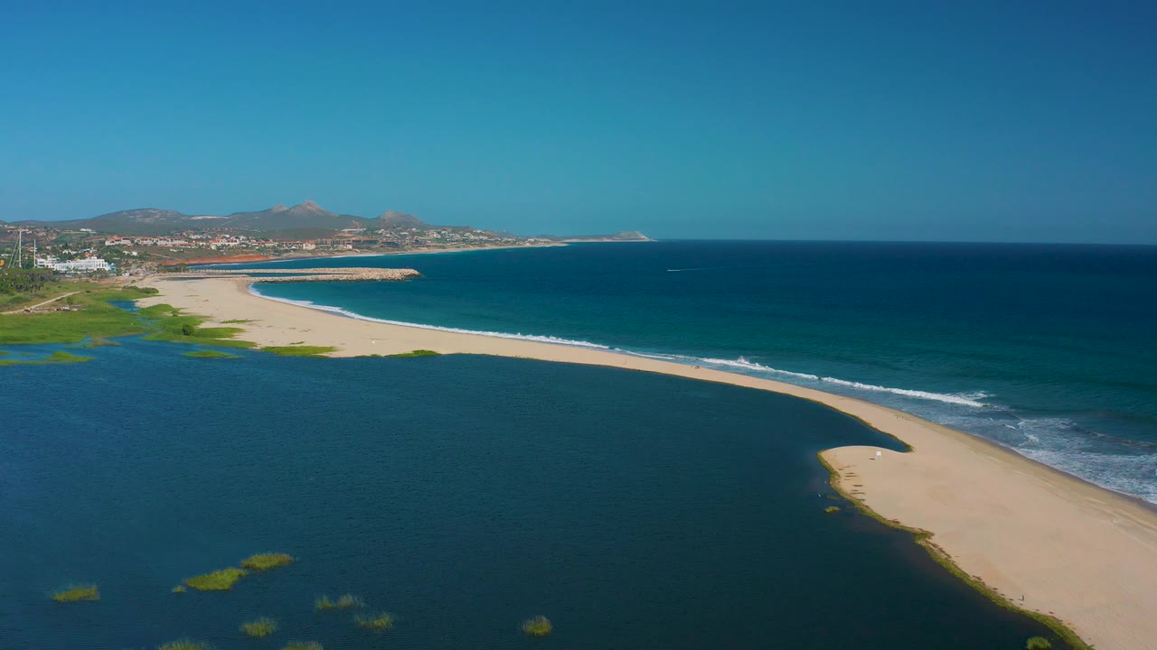 Sandy shoreline curves between dark lagoon water and blue ocean.