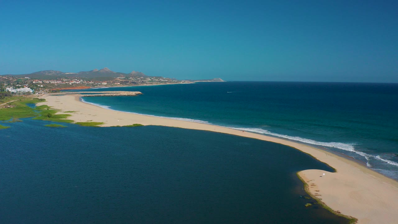 Aerial view in San Jose Del Cabo, Mexico, with a pale sandy spit separating a dark lagoon from blue ocean and no visible people.