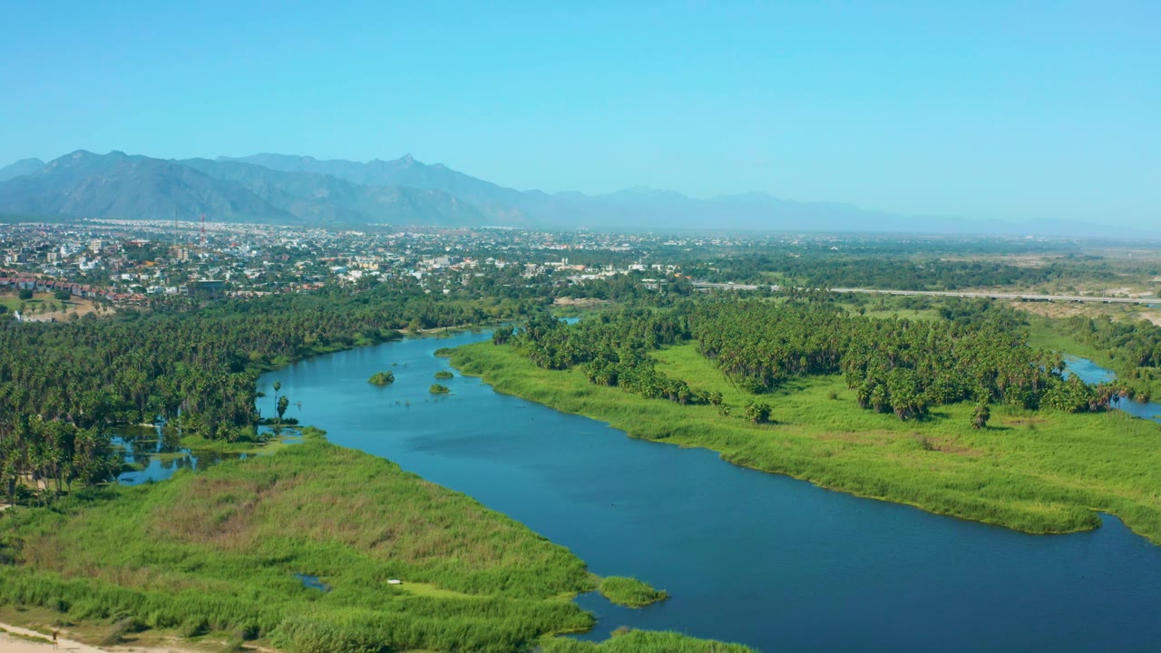 River channel crossing a green valley below a distant town.