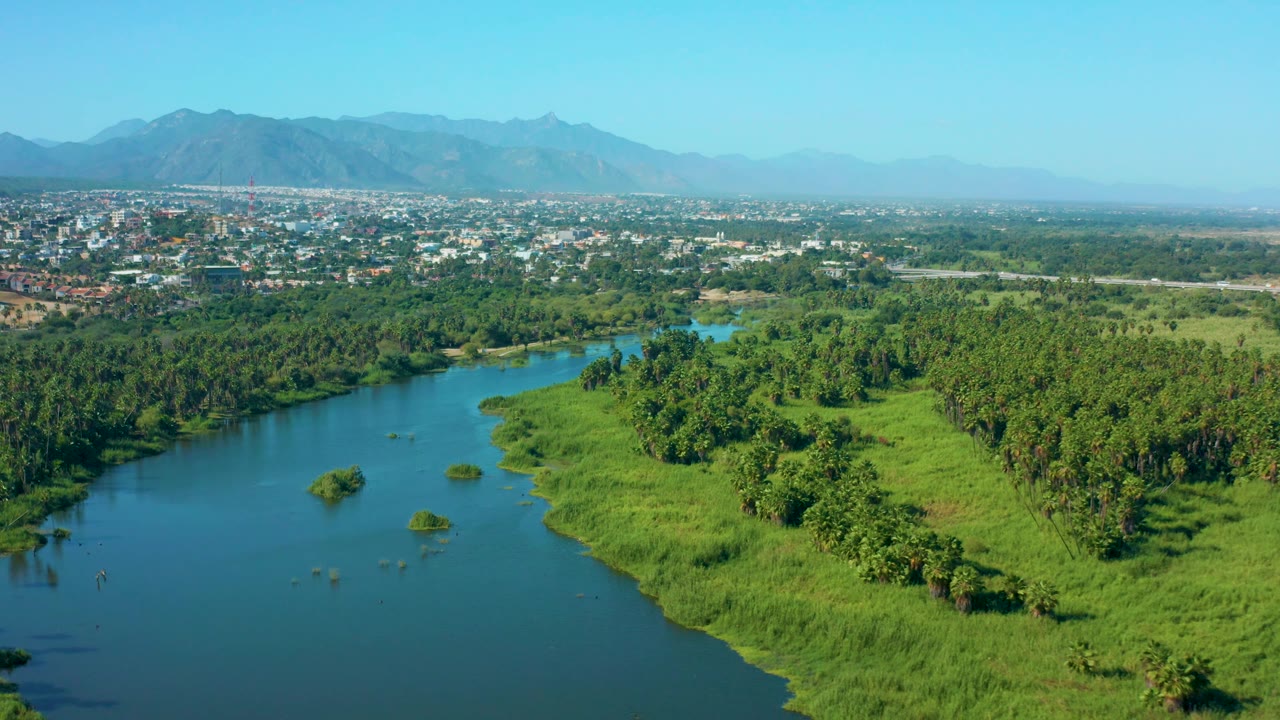 Aerial landscape with river, green wetlands, city buildings, and mountains.