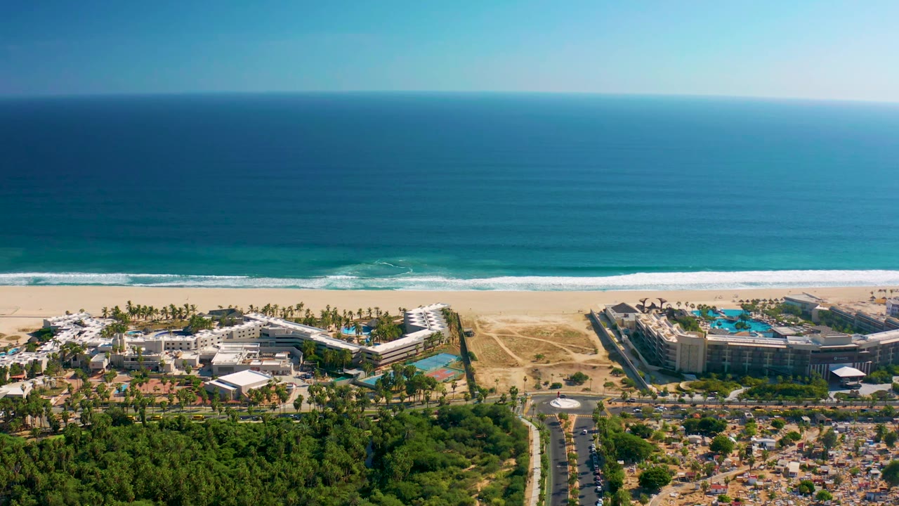 Aerial coastal view with resort buildings beside a sandy beach and blue ocean.