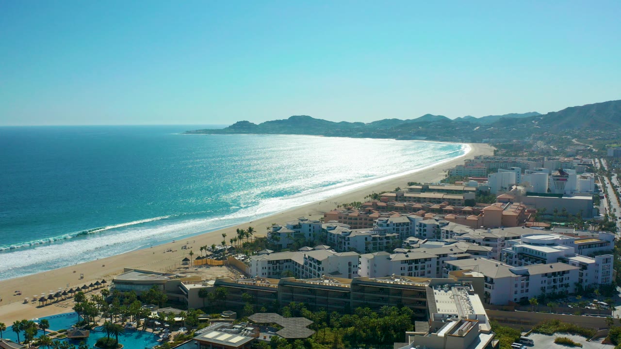 Aerial view of ocean, sandy beach, resort buildings, and distant mountains.