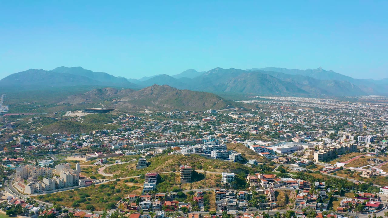 Aerial view of hillside buildings, city blocks, distant mountains, and clear sky.