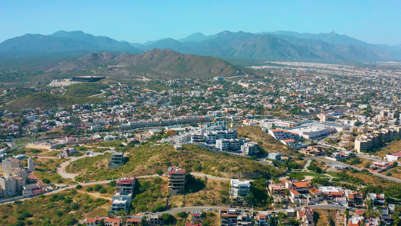 Drone-height cityscape with hillside roads and mountains under blue sky.