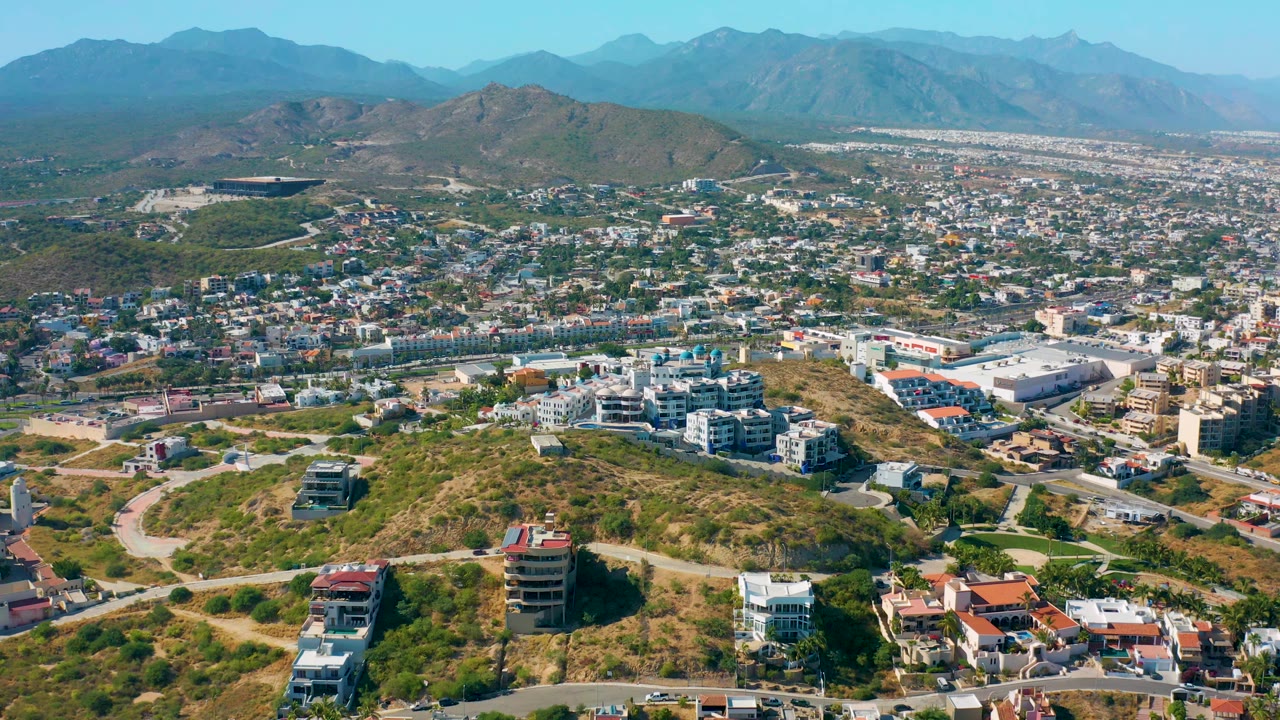 High drone view across hillside buildings, roads, city, and distant mountains