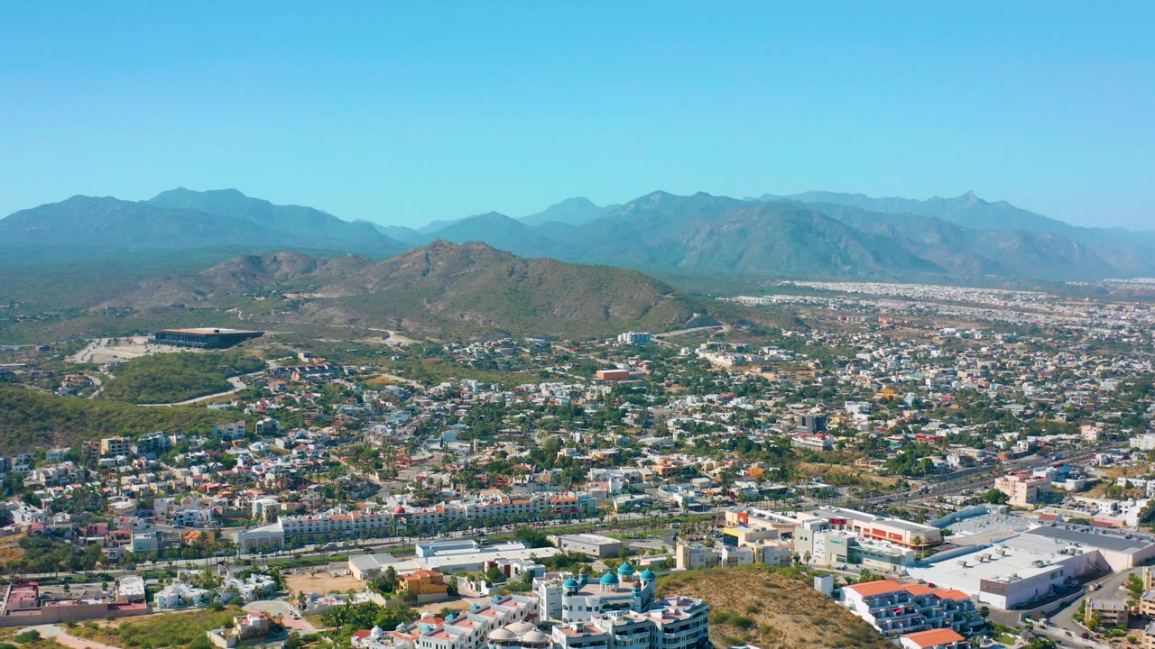 High aerial view with city foreground, hills, and mountains under clear sky.