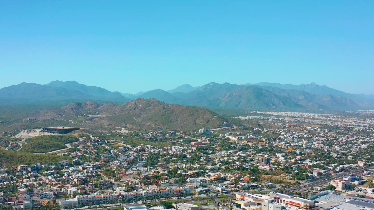 Aerial panorama of city blocks, green hills, and distant mountain ridges