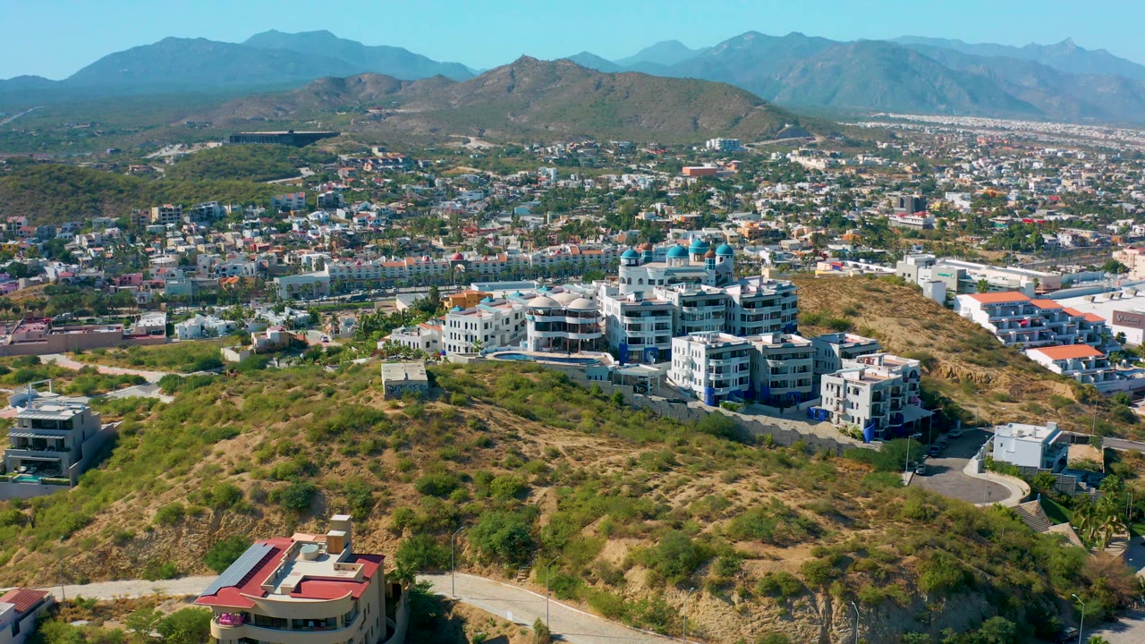 Wide elevated view of hillside homes and a city below mountains.
