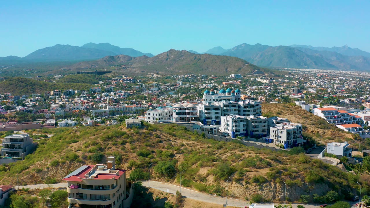 Elevated view across hillside vegetation, homes, city rooftops, and distant mountains.
